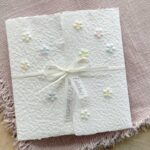 Handgeschöpfte Einladungskarte mit geprägten Blümchen im Gatefold-Design, mit Satinschleife und Büttenrand