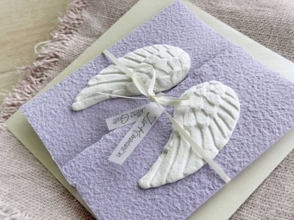 Seitliche Ansicht Glückwunschkarte aus handgeschöpftem Papier mit weissen Engelsflügeln auf lila Karte im Gatefold Design. Personalisierbar, hergestellt in meiner kleinen Manufaktur in der Schweiz.