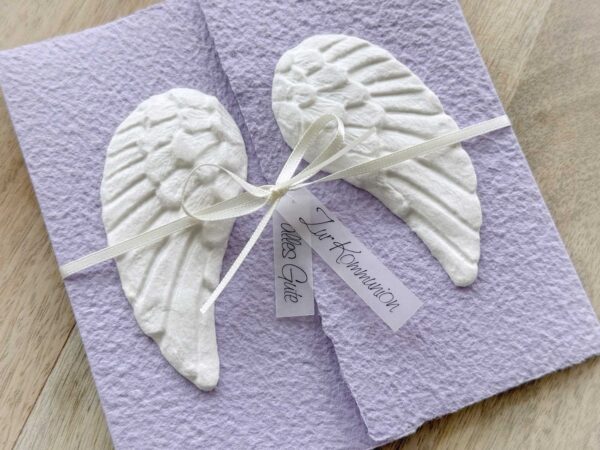 Nahaufnahme Glückwunschkarte aus handgeschöpftem Papier mit weissen Engelsflügeln auf lila Karte im Gatefold Design. Personalisierbar, hergestellt in meiner kleinen Manufaktur in der Schweiz.