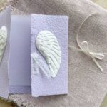 Geöffnete Glückwunschkarte aus handgeschöpftem Papier mit weissen Engelsflügeln auf lila Karte im Gatefold Design. Personalisierbar, hergestellt in meiner kleinen Manufaktur in der Schweiz.
