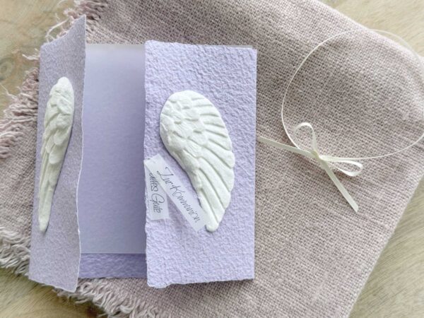 Geöffnete Glückwunschkarte aus handgeschöpftem Papier mit weissen Engelsflügeln auf lila Karte im Gatefold Design. Personalisierbar, hergestellt in meiner kleinen Manufaktur in der Schweiz.