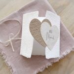 Geöffnete Ansicht Glückwunschkarte zur Hochzeit aus handgeschöpftem Papier im Gatefold Design. Mit einem Doppelherz aus zwei verschiedenen beige-tönen und Titel "Just Married". Verschluss mit einem Satinband in creme.