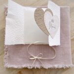 Aufgeklappte Glückwunschkarte zur Hochzeit aus handgeschöpftem Papier im Gatefold Design. Mit einem Doppelherz aus zwei verschiedenen beige-tönen und Titel "Just Married". Verschluss mit einem Satinband in creme.