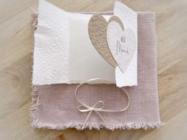 Aufgeklappte Glückwunschkarte zur Hochzeit aus handgeschöpftem Papier im Gatefold Design. Mit einem Doppelherz aus zwei verschiedenen beige-tönen und Titel "Just Married". Verschluss mit einem Satinband in creme.