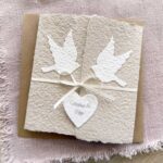 Personalisierte Glückwunschkarte zur Hochzeit im Gatefold Design. Handgeschöpftes, beiges Papier mit zwei weissen Tauben die aufeinander zu fliegen. 