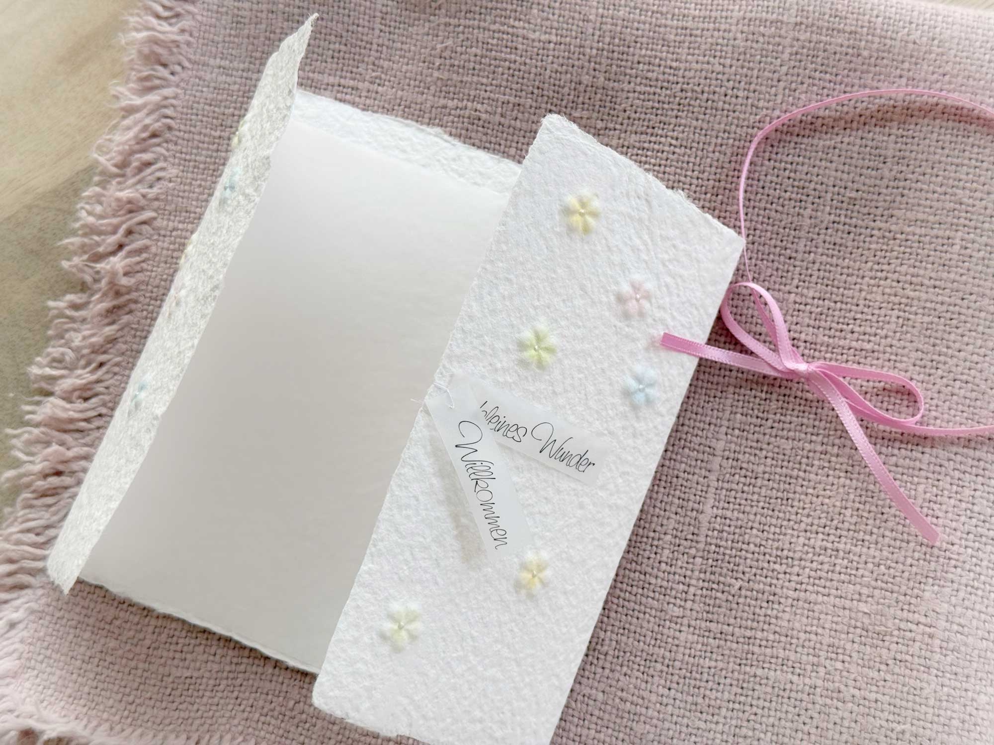 Geöffnete Gatefold Karte aus handgeschöpftem Papier mit geprägten Blümchen, handbemalt in zarten pastell Farben.