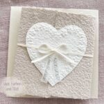 Personalisierte Hochzeitseinladung Blumenherz aus handgeschöpftem Büttenpapier mit floraler Herzprägung und Titelstreifen am Satinband