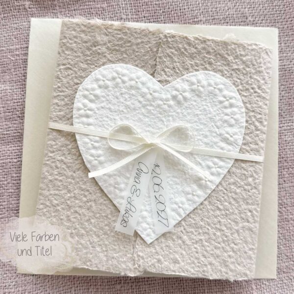Personalisierte Hochzeitseinladung Blumenherz aus handgeschöpftem Büttenpapier mit floraler Herzprägung und Titelstreifen am Satinband