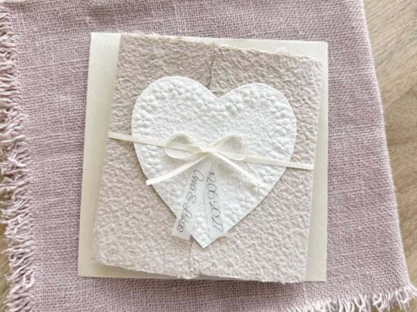 Personalisierte Hochzeitseinladung Blumenherz aus handgeschöpftem Büttenpapier mit floraler Herzprägung und Titelstreifen am Satinband