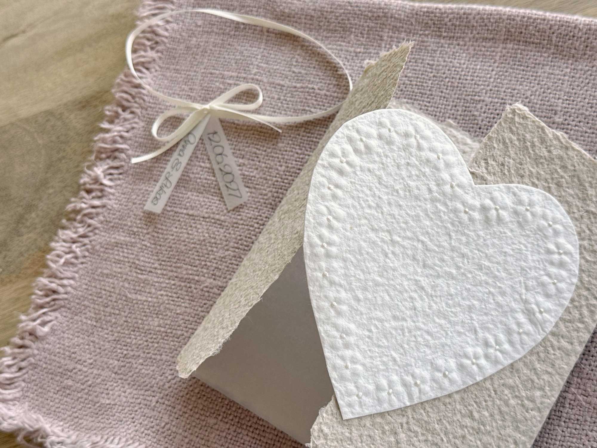 Personalisierte Gatefold Hochzeitseinladung Blumenherz aus handgeschöpftem Büttenpapier mit floraler Herzprägung und Titelstreifen am Satinband