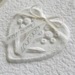 Nahaufnahme Hochzeitseinladung "Büttenherz" aus handgeschöpftem Papier weiss in weiss. Mit personalisiertem Titel auf zwei transparentpapierstreifen.