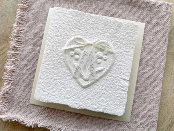 Hochzeitseinladung "Büttenherz" aus handgeschöpftem Papier weiss in weiss. Mit personalisiertem Titel auf zwei transparentpapierstreifen.