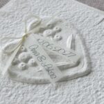 Seitliche Nahaufnahme Hochzeitseinladung "Büttenherz" aus handgeschöpftem Papier weiss in weiss. Mit personalisiertem Titel auf zwei transparentpapierstreifen.