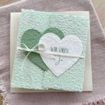Personalisierbare Gatefold-Hochzeitseinladung aus handgeschöpftem Papier in zartem Grün mit zwei herzen in dunkelgrün und weiss. Titel "Wir sagen Ja".