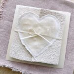 Hochzeitseinladung aus handgeschöpftem Papier mit edlem, handgefilztem Perlenherz als Motiv. Gatefold Design mit Satinband verschlossen.
