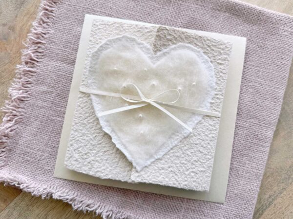 Hochzeitseinladung aus handgeschöpftem Papier mit edlem, handgefilztem Perlenherz als Motiv. Gatefold Design mit Satinband verschlossen.