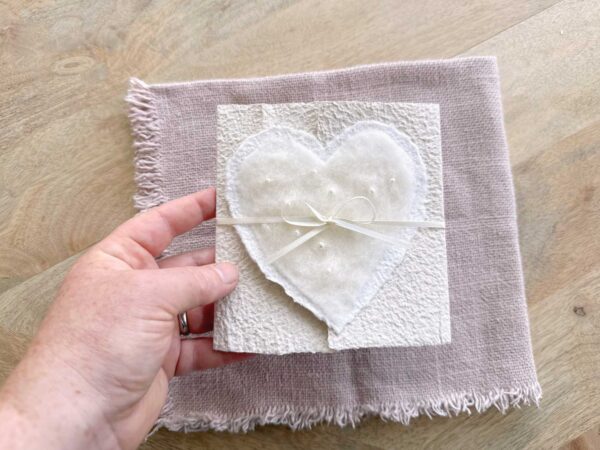 Grössenansicht Hochzeitseinladung aus handgeschöpftem Papier mit edlem, handgefilztem Perlenherz als Motiv. Gatefold Design mit Satinband verschlossen.