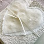 Nahaufnahme Hochzeitseinladung aus handgeschöpftem Papier mit edlem, handgefilztem Perlenherz als Motiv. Gatefold Design mit Satinband verschlossen.