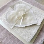 Seitliche Ansicht Hochzeitseinladung aus handgeschöpftem Papier mit edlem, handgefilztem Perlenherz als Motiv. Gatefold Design mit Satinband verschlossen.