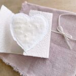Geöffnete Hochzeitseinladung aus handgeschöpftem Papier mit edlem, handgefilztem Perlenherz als Motiv.