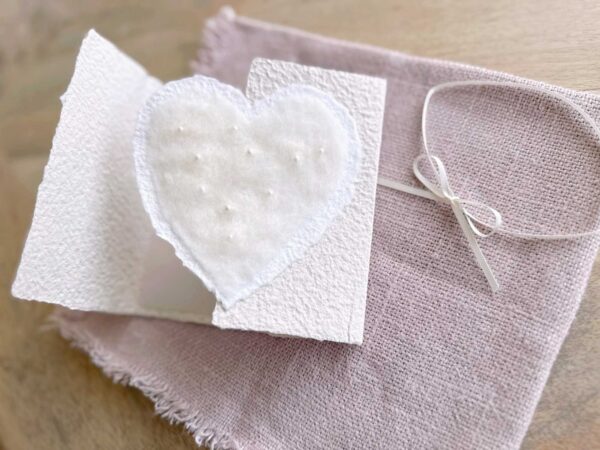 Geöffnete Hochzeitseinladung aus handgeschöpftem Papier mit edlem, handgefilztem Perlenherz als Motiv.