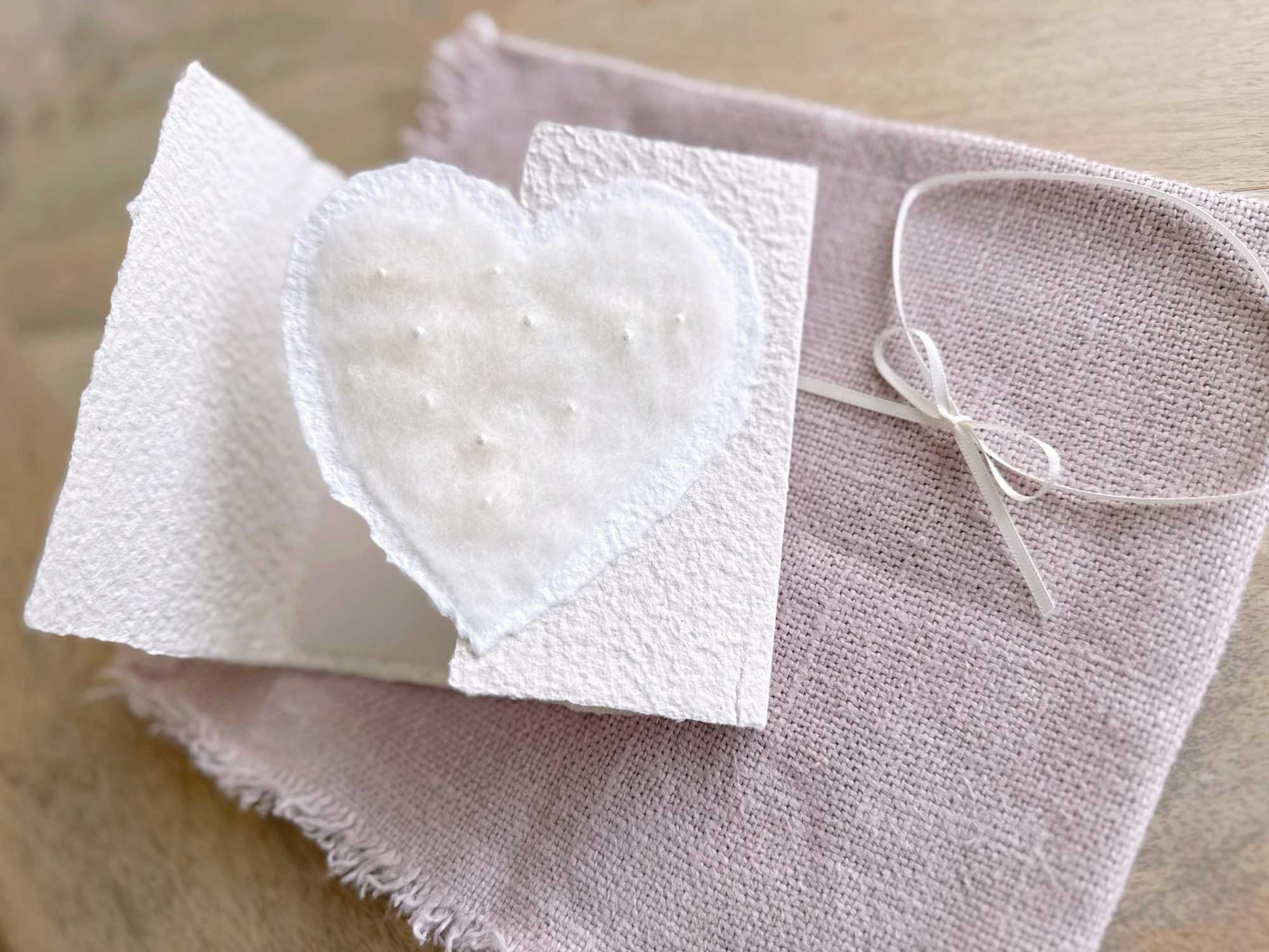 Geöffnete Hochzeitseinladung aus handgeschöpftem Papier mit edlem, handgefilztem Perlenherz als Motiv.