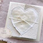Personalisierte Hochzeitseinladung aus handgeschöpftem Papier mit edlem, handgefilztem Perlenherz als Motiv. Gatefold Design mit Satinband verschlossen.