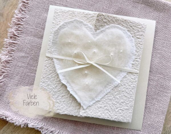 Personalisierte Hochzeitseinladung aus handgeschöpftem Papier mit edlem, handgefilztem Perlenherz als Motiv. Gatefold Design mit Satinband verschlossen.