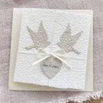 Hochzeitseinladung «Tauben» aus handgeschöpftem Büttenpapier im Gatefold Desing mit zwei beigen Tauben und elegantem Satinband. Personalisierter Titel auf beigem Herz.