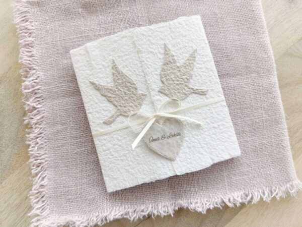 Besondere Hochzeitseinladung «Tauben» aus handgeschöpftem Büttenpapier im Altarfalz Desing mit zwei beigen Tauben und elegantem Satinband. Personalisierter Titel auf beigem Herz.