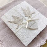 Seitliche Ansicht einer Hochzeitseinladung «Tauben» aus handgeschöpftem Papier im Gatefold Desing mit zwei beigen Tauben und elegantem Satinband. Personalisierter Titel auf beigem Herz.