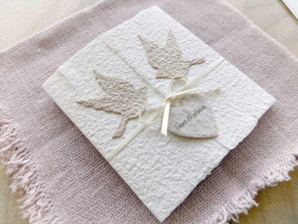 Seitliche Ansicht einer Hochzeitseinladung «Tauben» aus handgeschöpftem Papier im Gatefold Desing mit zwei beigen Tauben und elegantem Satinband. Personalisierter Titel auf beigem Herz.