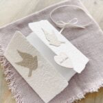 Aufgeklappte Hochzeitseinladung «Tauben» aus handgeschöpftem Papier mit Altarfalz. Motiv sind zwei beigen Tauben. Personalisierter Titel auf beigem Herz.