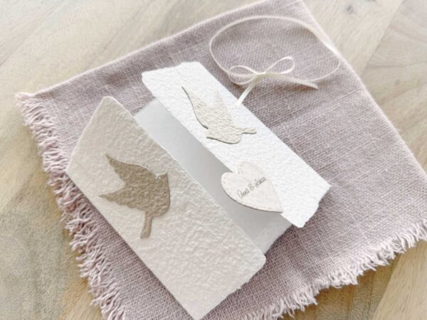 Aufgeklappte Hochzeitseinladung «Tauben» aus handgeschöpftem Papier mit Altarfalz. Motiv sind zwei beigen Tauben. Personalisierter Titel auf beigem Herz.