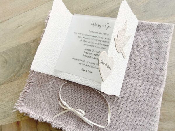 Geöffnete Ansicht einer Hochzeitseinladung «Tauben» aus handgeschöpftem Büttenpapier im Gatefold Desing mit zwei beigen Tauben und elegantem Satinband. Mit Beispieltext für bedrucktes Einlegeblatt