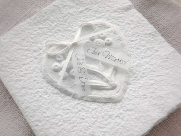 Nahaufnahme personalisierte Glückwunschkarte zur Hochzeit aus handgeschöpftem Papier. Mit einem 3D-Herz aus einem Springerle Herz, welches zwei Blumen aus einer Wurzel zeigt. In der edlen Hochzeitskombination "weiss in weiss".