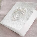 Geöffnete Ansicht Glückwunschkarte zur Hochzeit aus handgeschöpftem Papier. Mit einem 3D-Herz aus einem Springerle Herz, welches zwei Blumen aus einer Wurzel zeigt. In der edlen Hochzeitskombination "weiss in weiss".