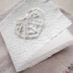 Glückwunschkarte zur Hochzeit aus handgeschöpftem Papier. Mit einem 3D-Herz aus einem Springerle Herz, welches zwei Blumen aus einer Wurzel zeigt. In der edlen Hochzeitskombination "weiss in weiss".