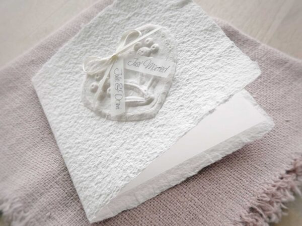 Glückwunschkarte zur Hochzeit aus handgeschöpftem Papier. Mit einem 3D-Herz aus einem Springerle Herz, welches zwei Blumen aus einer Wurzel zeigt. In der edlen Hochzeitskombination "weiss in weiss".