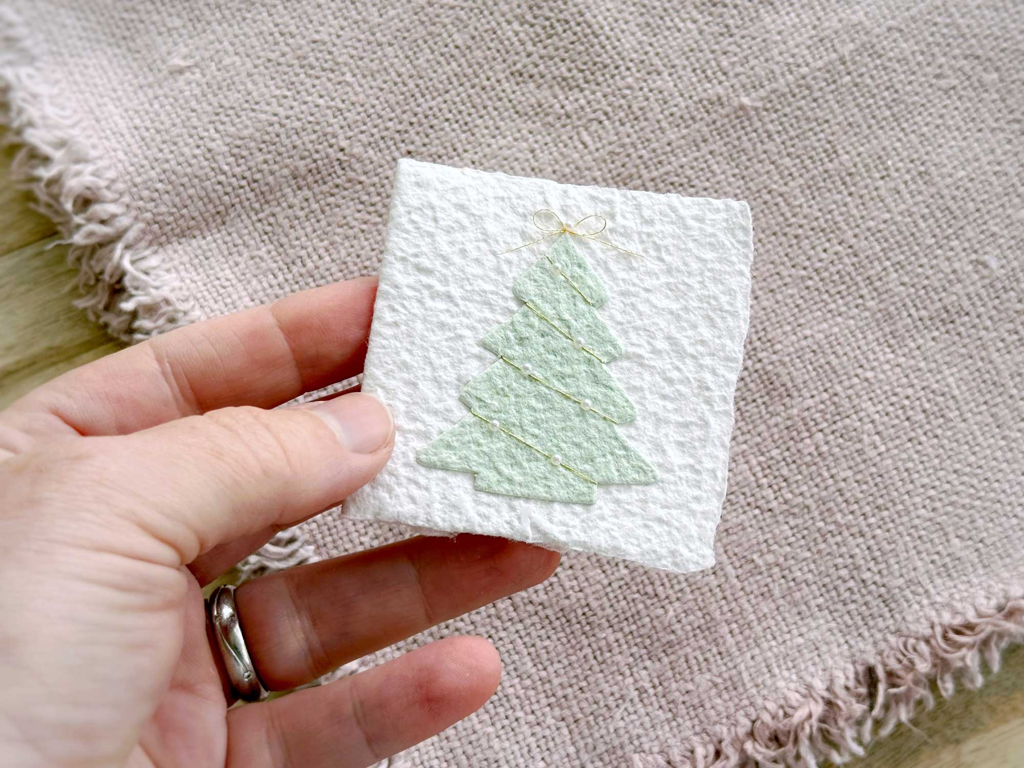 Kleine Weihnachtskarte Tannenbaum aus handgeschöpftem Papier in einer Hand – Format ca. 6,5 × 6,5 cm