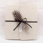 Trauerkarte aus handgeschöpftem Papier in beige mit einer Feder, Titelstreifen und Satinschleifchen