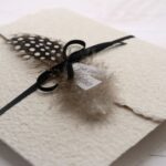 Trauerkarte aus handgeschöpftem Papier in beige mit einer Feder, Titelstreifen und Satinschleifchen