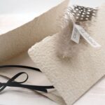 Trauerkarte aus handgeschöpftem Papier in beige mit einer Feder, Titelstreifen und Satinschleifchen