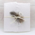 Trauerkarte aus handgeschöpftem Papier in weiss mit einer Feder, Titelstreifen und Satinschleifchen