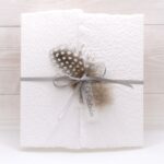 Trauerkarte aus handgeschöpftem Papier in weiss mit einer Feder, Titelstreifen und Satinschleifchen