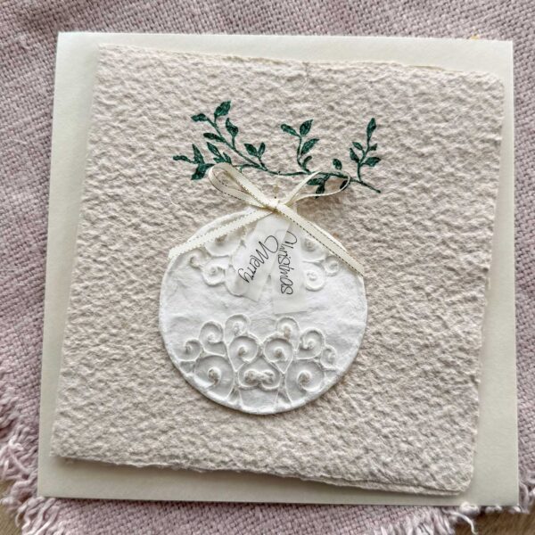 Personalisierbare Weihnachtskarte Weihnachtskugel aus handgeschöpftem Büttenpapier mit reliefartigem Kugelmotiv, grünem Zweig und cremefarbener Satinschleife.
